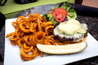 Grilled elk burger with fresh sliced jalapeno peppers and seasoned curly fries